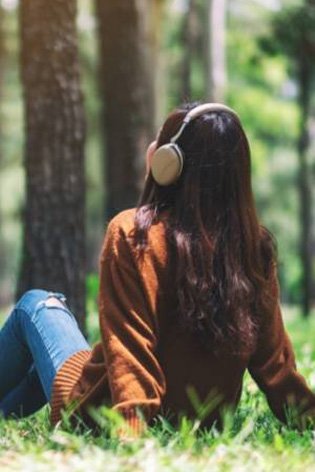 Woman sat down on the grass, with headphones on 